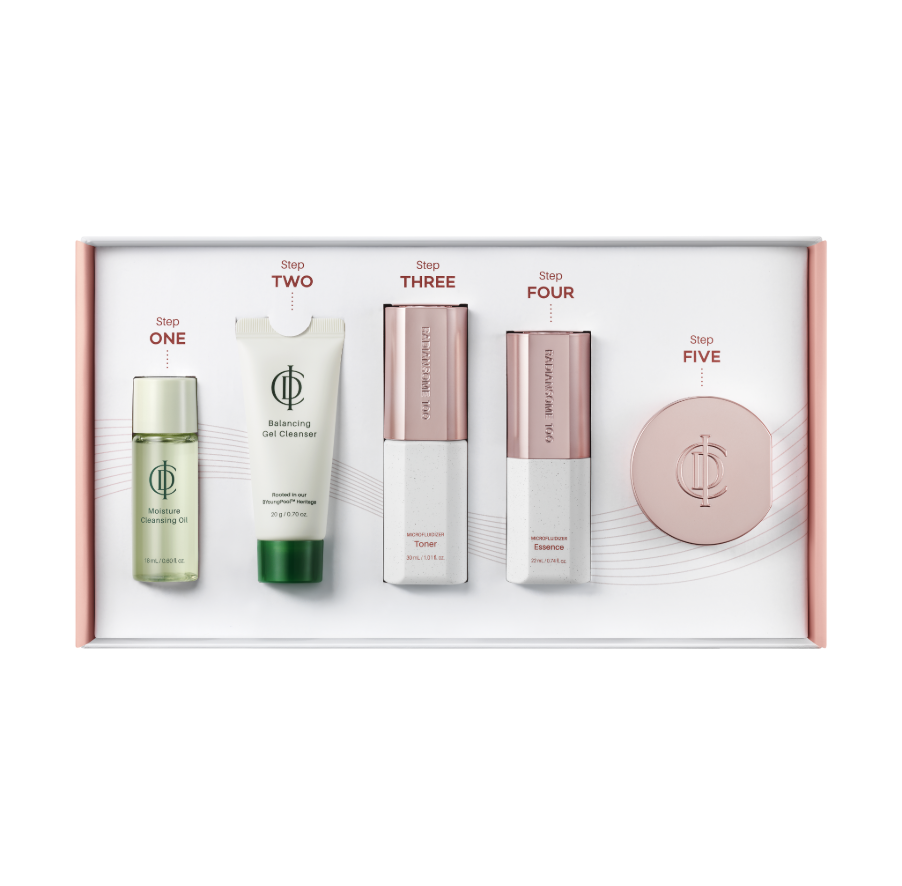 A five-step skincare set in a white presentation box with pink trim, featuring a green oil, a white tube, and three rose-gold and white bottles, labeled Step One through Step Five.