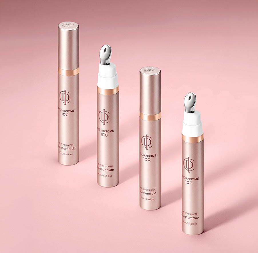 Four cosmetic tubes from the brand RADIANSOME 100 in a metallic rose gold finish, arranged on a soft pink background. Two tubes are open, showing white caps with silver applicator tips, and two are closed.